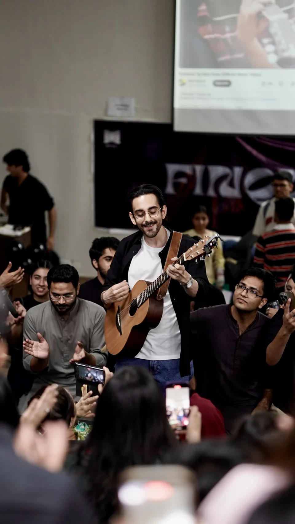 Bilal Khan playing acoustic guitar surrounded by an audience