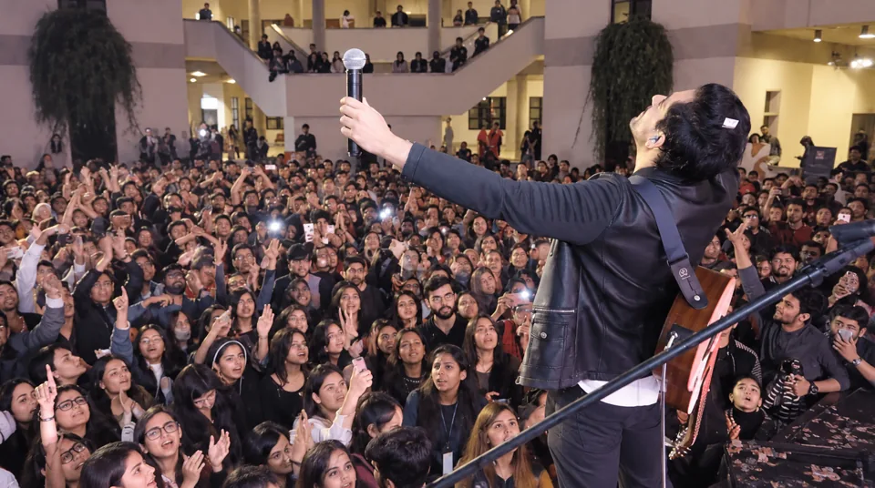 Bilal Khan on stage with an acoustic guitar, facing a packed university audience